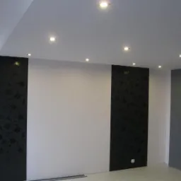 Pokój po remoncie z białymi ścianami, czarnymi panelami dekoracyjnymi z motywem kwiatowym i podwieszanym sufitem z punktowym oświetleniem LED.