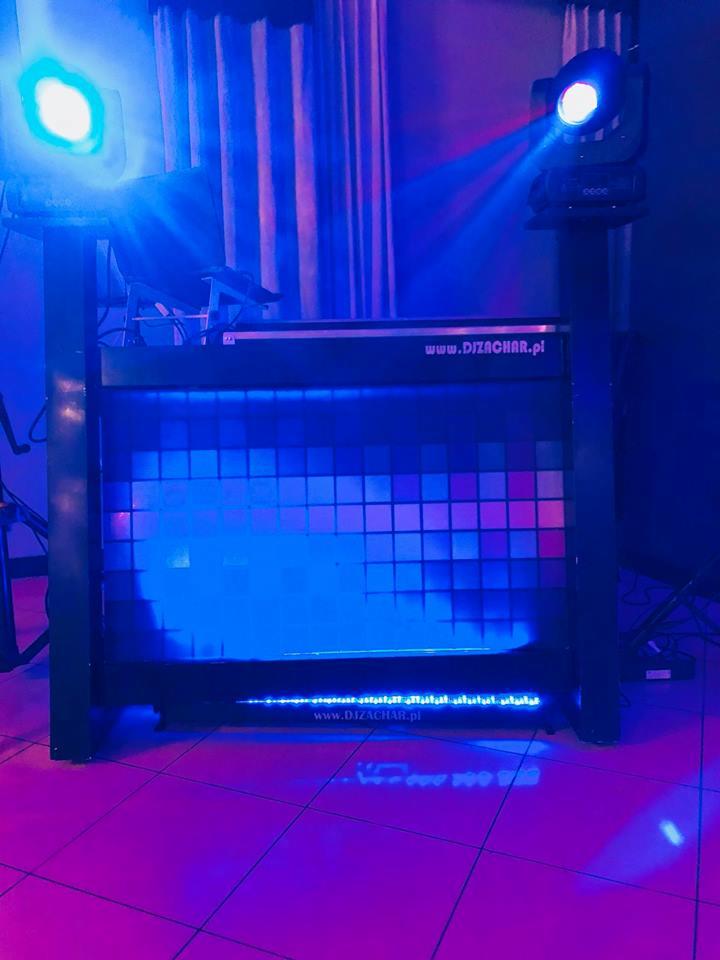 Stanowisko DJ'a z podświetlanym panelem i dwoma reflektorami skierowanymi w górę, widoczny adres strony internetowej na panelu i podłodze.