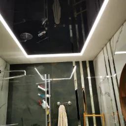 Nowoczesna łazienka z czarnym, lustrzanym sufitem podwieszanym z oświetleniem LED, szklaną kabiną prysznicową i marmurowymi płytkami.