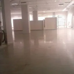 Błyszcząca, świeżo wylana posadzka w rozległym, jasnym pomieszczeniu z kolumnami. Widoczne elementy konstrukcyjne sufitu i drabina w tle.