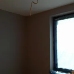 Świeżo pomalowane wnętrze w Dabrowie Gorniczej, widoczne zabezpieczone okno i wystający kabel ze ściany.