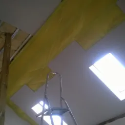 Montaż sufitu podwieszanego z widoczną izolacją i oknem dachowym, wsparty na metalowej konstrukcji i drewnianym słupie, z drabiny