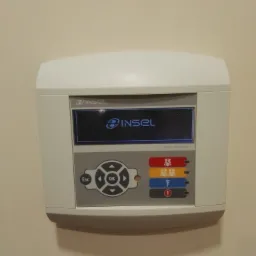 Panel sterowania systemem alarmowym INSEL zamontowany na beżowej ścianie, widoczne przyciski funkcyjne i wyświetlacz z logo.