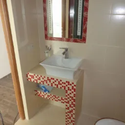 Umywalka nablatowa w kwadratowej szafce z czerwono-białą mozaiką, dopasowane lustro z oświetleniem LED w łazience z beżowymi płytkami.