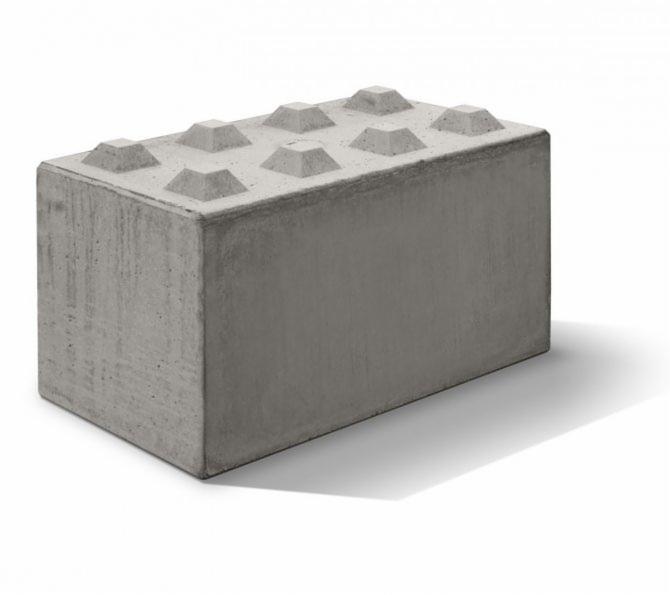 Szary, betonowy blok z wypustkami na górnej powierzchni, przypominający duży klocek, o surowej fakturze betonu.