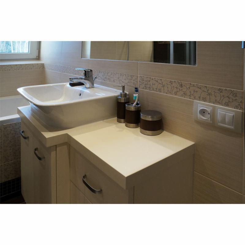 Wykończona łazienka z kremowymi płytkami z motywem roślinnym, białą umywalką nablatową na szafce z szufladami i akcesoriami łazienkowymi w brązowych pojemnikach.