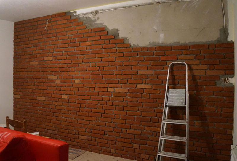 Ceglana ściana w trakcie montażu, widoczne fragmenty surowego muru i drabina oparta o ścianę.