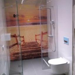 Vik-Bud - Szklana kabina prysznicowa z motywem plaży i zachodu słońca na ścianie, wisząca toaleta, szare płytki podłogowe i ścienne, nowoczesna aranżacja łazienki.