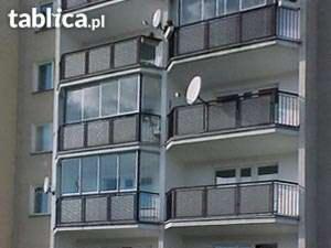 Zewnętrzny widok na balkony w bloku mieszkalnym. Część balkonów zabudowana szklaną konstrukcją, tworzącą ogrody zimowe. Na niektórych balkonach widoczne anteny satelitarne.