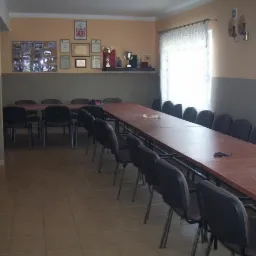 Wnętrze sali konferencyjnej z długim stołem i rzędem krzeseł, na ścianie dyplomy i trofea.