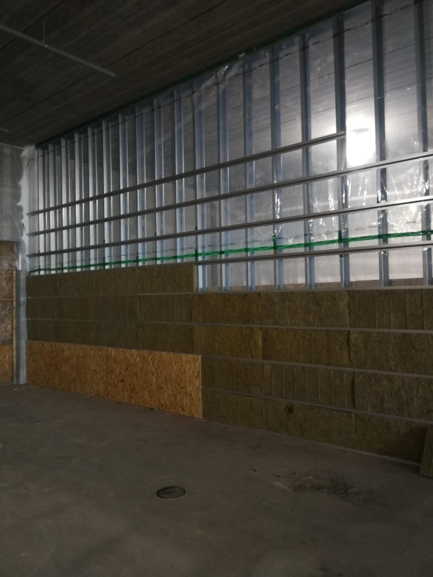 Montaż izolacji z wełny mineralnej w metalowym stelażu ściany działowej, częściowo obłożonej płytami OSB.