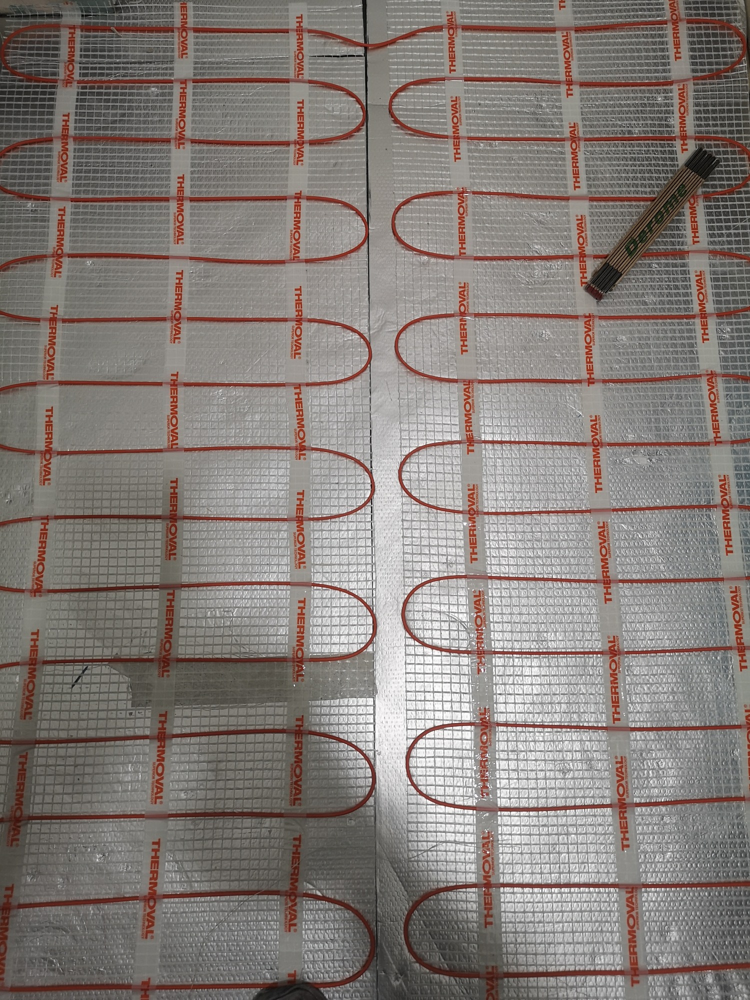 Mata grzewcza podłogowa marki Thermoval rozłożona na srebrnej folii izolacyjnej, widoczna składana miarka stolarska.