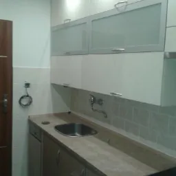 Nowoczesna kuchnia z białymi szafkami górnymi z matowymi szybami, szarym blatem i srebrną armaturą, widok na zlewozmywak i fragment płyty grzewczej.