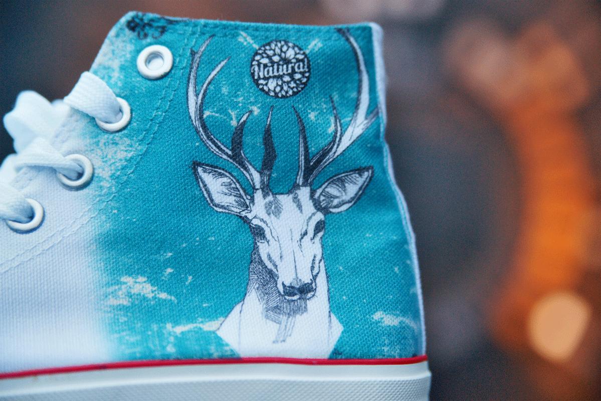Turkusowy but sportowy z nadrukiem głowy jelenia i logo 'Natura!', białe sznurówki, czerwona linia na podeszwie, widok z bliska.