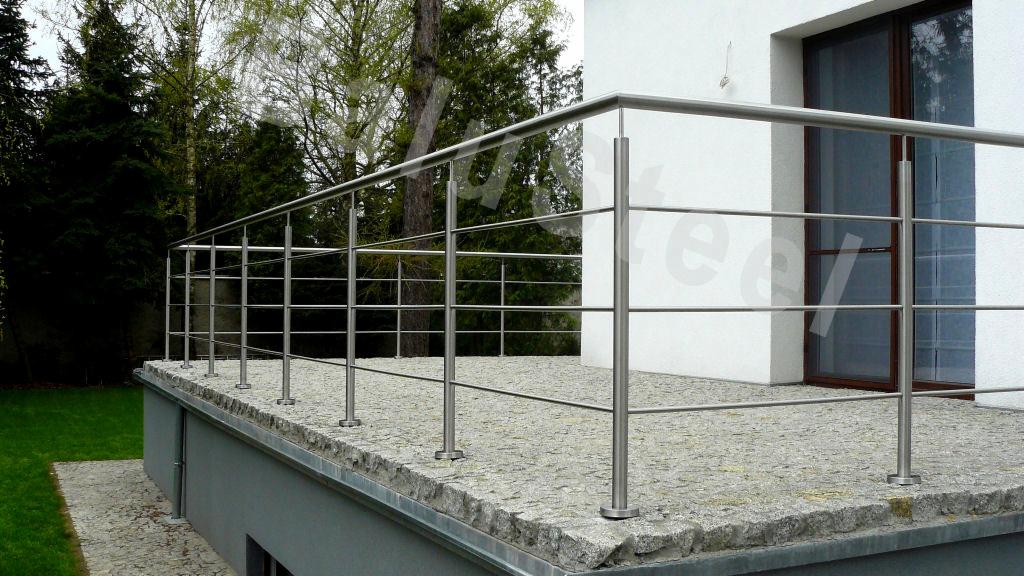 Zewnętrzna balustrada ze stali szlifowanej, zamontowana na tarasie wyłożonym kamienną kostką, z widokiem na trawnik i drzewa.
