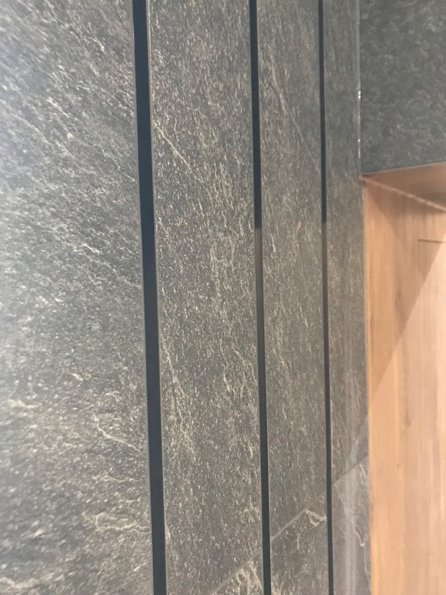 Nowoczesna ściana wykończona szarymi płytami kamiennymi z ciemnymi fugami, widoczny fragment drewnianej zabudowy w Mszanie Dolnej.