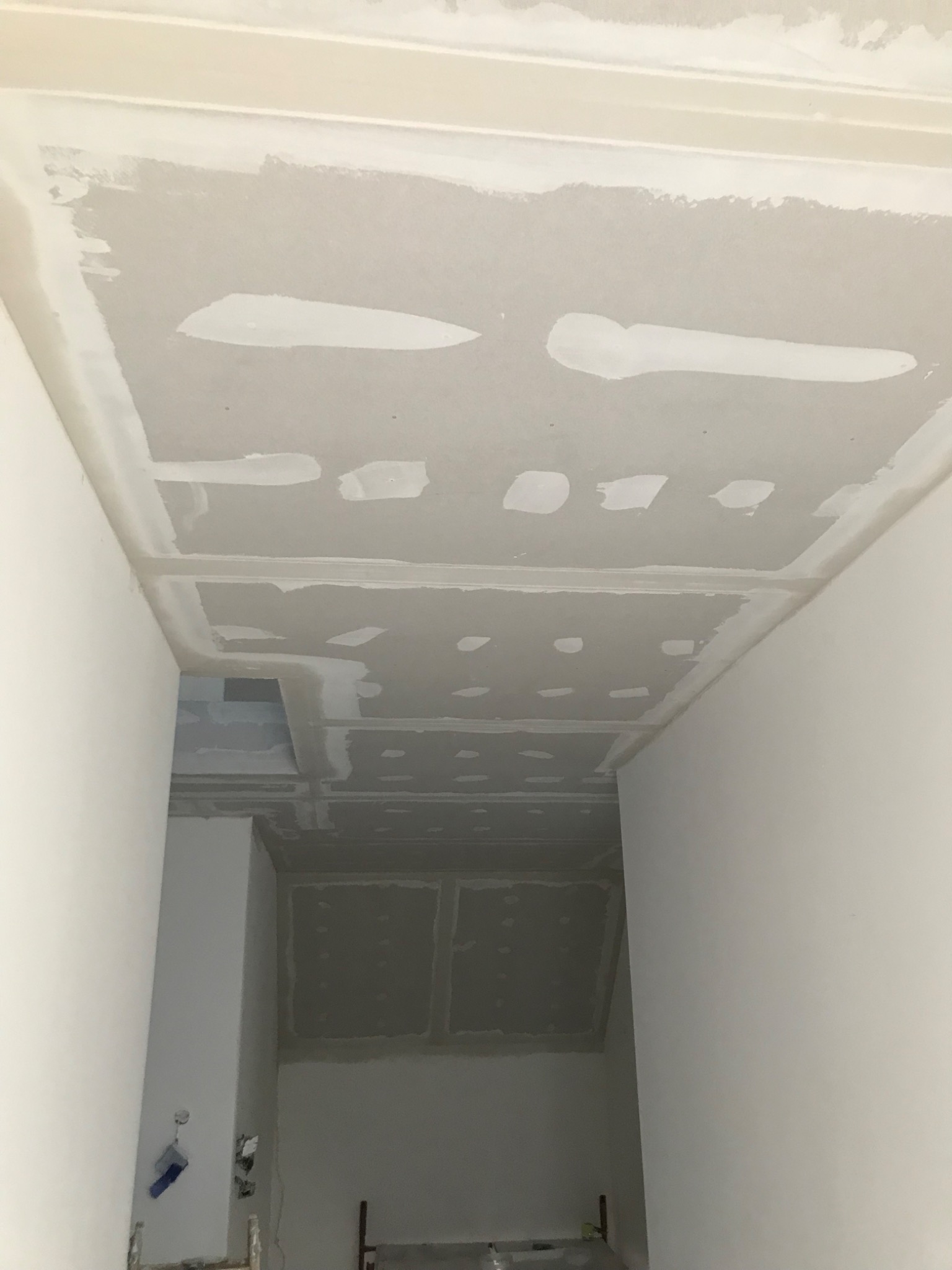 Sufit z płyt karton gipsowych w trakcie szpachlowania, widoczne łączenia i ślady po wkrętach, surowe wykończenie, fragment instalacji elektrycznej na ścianie.