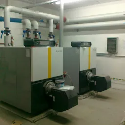 Dwa kotły grzewcze De Dietrich z żółtymi pasami, rury instalacyjne i puszka farby na jednym z kotłów, Kępno.