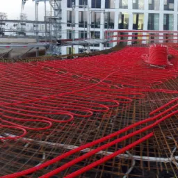 Czerwone rury w systemie instalacji grzewczej ułożone na zbrojeniu stropu w nowym budynku w trakcie budowy.