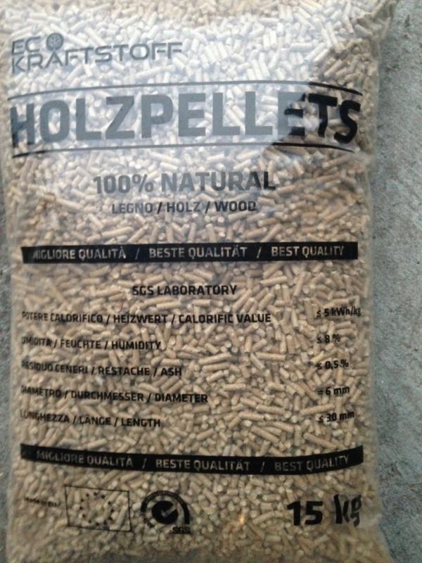 Worek z transparentnego tworzywa wypełniony jasnymi pelletami drzewnymi, widoczne oznaczenia 'HOLZPELLETS 100% NATURAL' oraz informacje o parametrach, waga 15 kg.