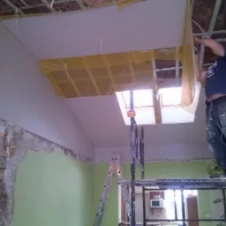 Montaż płyty gipsowej na suficie poddasza w Dobrem. Widoczne rusztowanie i okno dachowe.