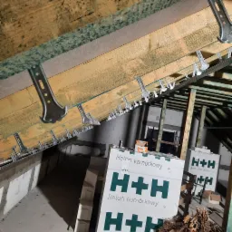 Montaż metalowych profili do drewnianej konstrukcji dachu pod płytę karton gips, widoczne paczki z betonem komórkowym H+H i fragment ściany z bloczków.