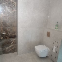 KBR Karol Reszka - Nowoczesna łazienka po remoncie: szare płytki imitujące kamień, podwieszana toaleta, marmurowa ściana pod prysznicem, minimalistyczny design.