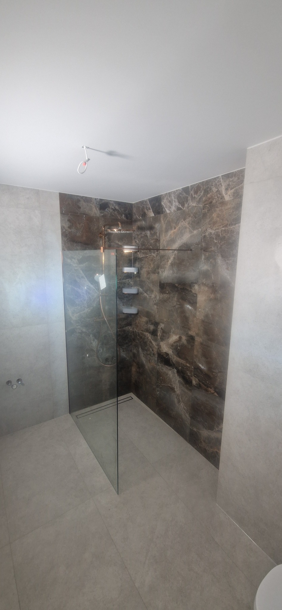 Nowoczesna kabina prysznicowa typu walk-in z marmurowymi płytkami w odcieniach brązu i szarości. Minimalistyczny design, szklana ścianka działowa i odpływ liniowy.