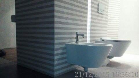 Nowoczesna łazienka z wiszącą miską WC i bidetem o minimalistycznym designie, na ścianach poziome pasy w odcieniach szarości, widoczne elementy instalacji wodnej.