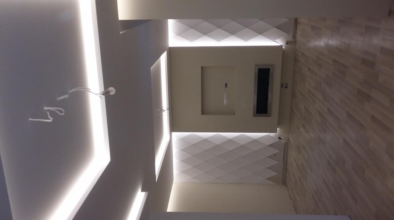 Sufit podwieszany z oświetleniem LED w kształcie rombów i listew w Obornikach, widoczne kable oświetleniowe przed montażem, parkiet na ścianie.