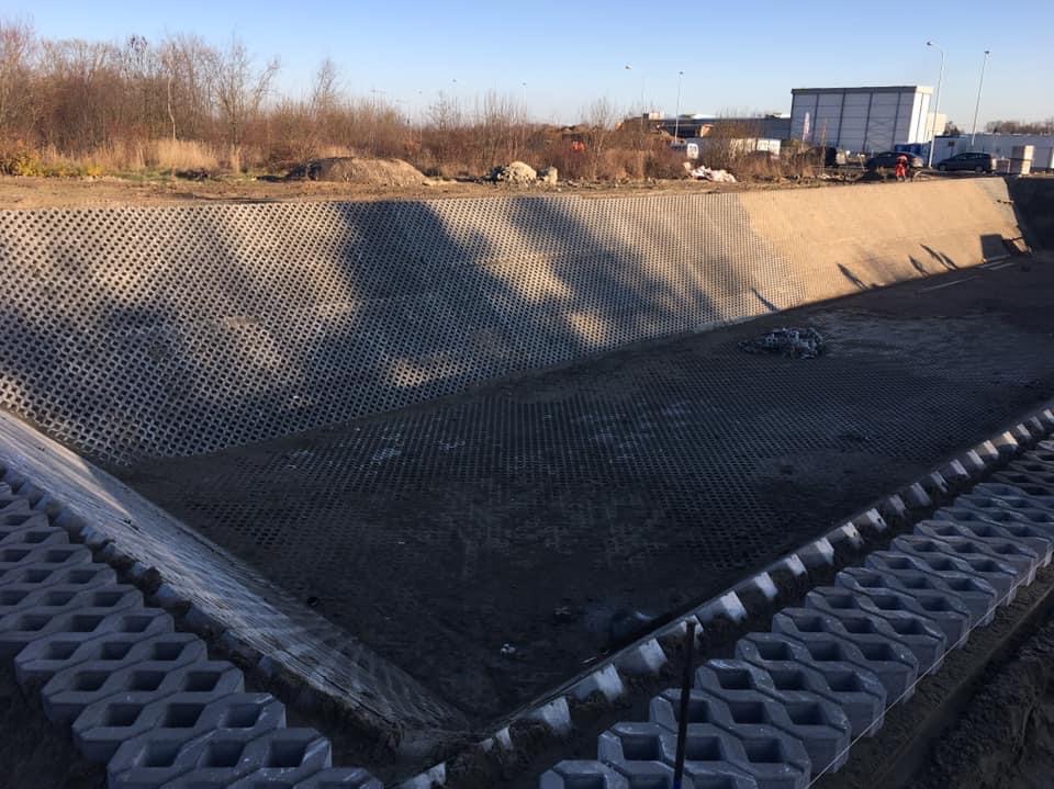 Wykonywanie utwardzenia terenu w Koluszkach z wykorzystaniem ażurowych płyt betonowych na skarpie i dnie rowu, z widocznymi elementami konstrukcyjnymi i ziemią.