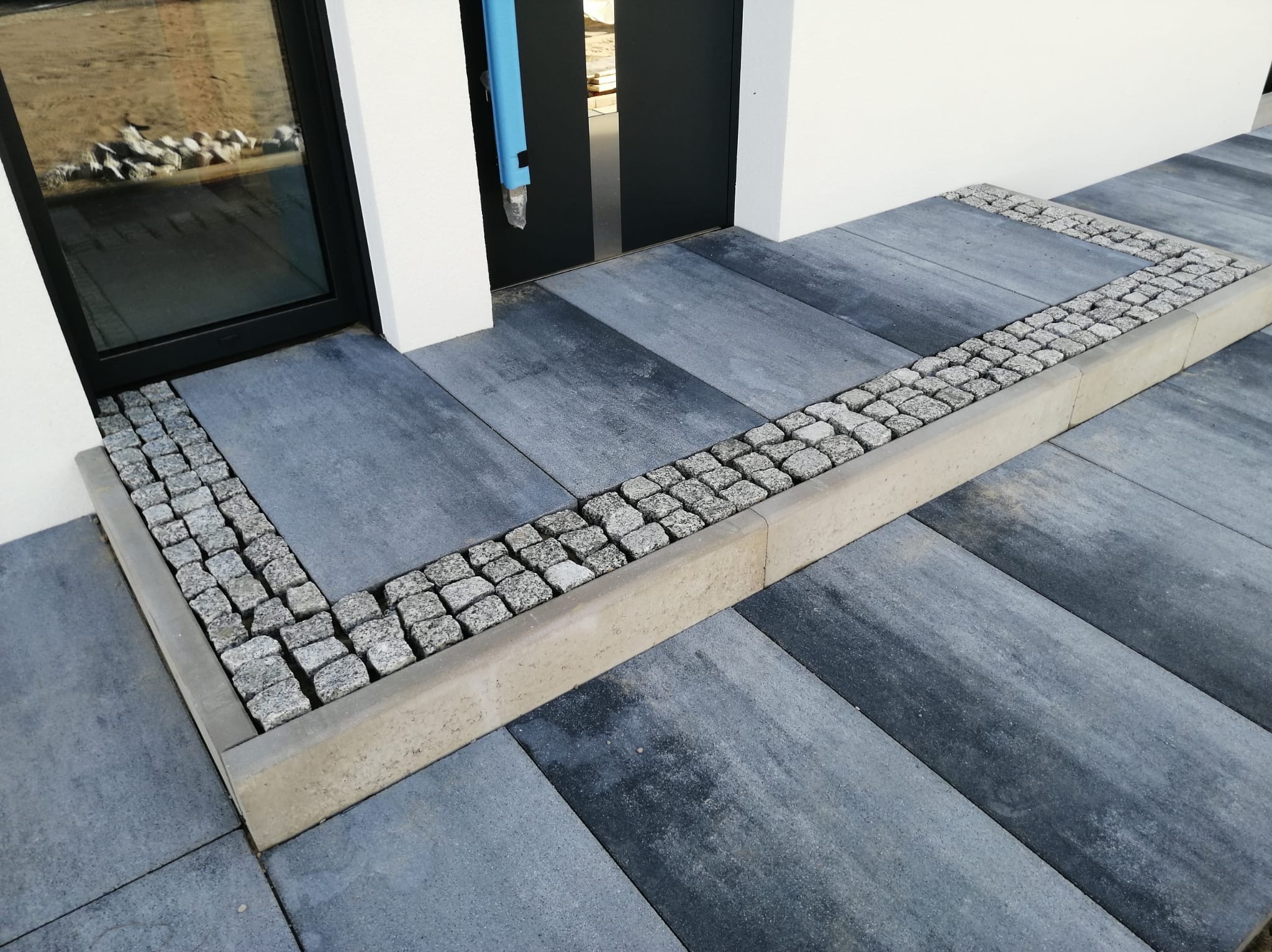 Nowoczesne wejście do domu z szarych płyt betonowych obramowanych kostką granitową i betonowym krawężnikiem, widok z góry.