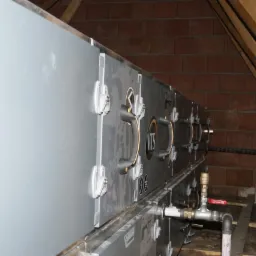 Instalacja rekuperacji VTS w przestrzeni poddasza z widocznymi elementami montażowymi, rurami i drewnianą konstrukcją dachu.