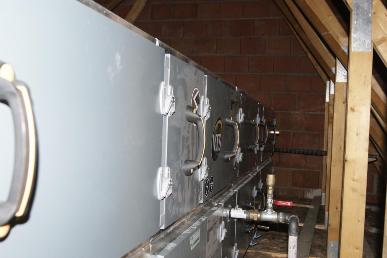 Instalacja rekuperacji VTS w przestrzeni poddasza z widocznymi elementami montażowymi, rurami i drewnianą konstrukcją dachu.