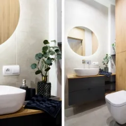 Nowoczesna łazienka w Konstantynowie Łódzkim z okrągłym lustrem podświetlanym LED, białą umywalką nablatową i czarną szafką pod umywalką. Uwagę zwraca drewniana zabudowa ściany z ukrytym systemem...