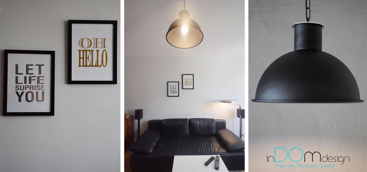 Salon z czarną skórzaną sofą, białym stolikiem kawowym, lampą wiszącą w stylu industrialnym i dekoracyjnymi plakatami w czarnych ramkach na ścianie.