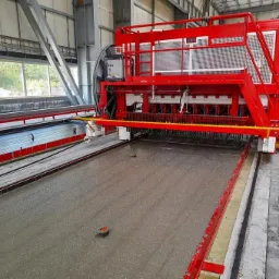 Czerwona maszyna do wylewania betonu w hali, z widocznym pracownikiem w kasku i świeżo wylaną, gładką powierzchnią betonu.