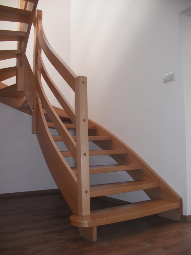 Jasne, drewniane schody kręcone z balustradą, widok z dołu, parkiet na podłodze, białe ściany.