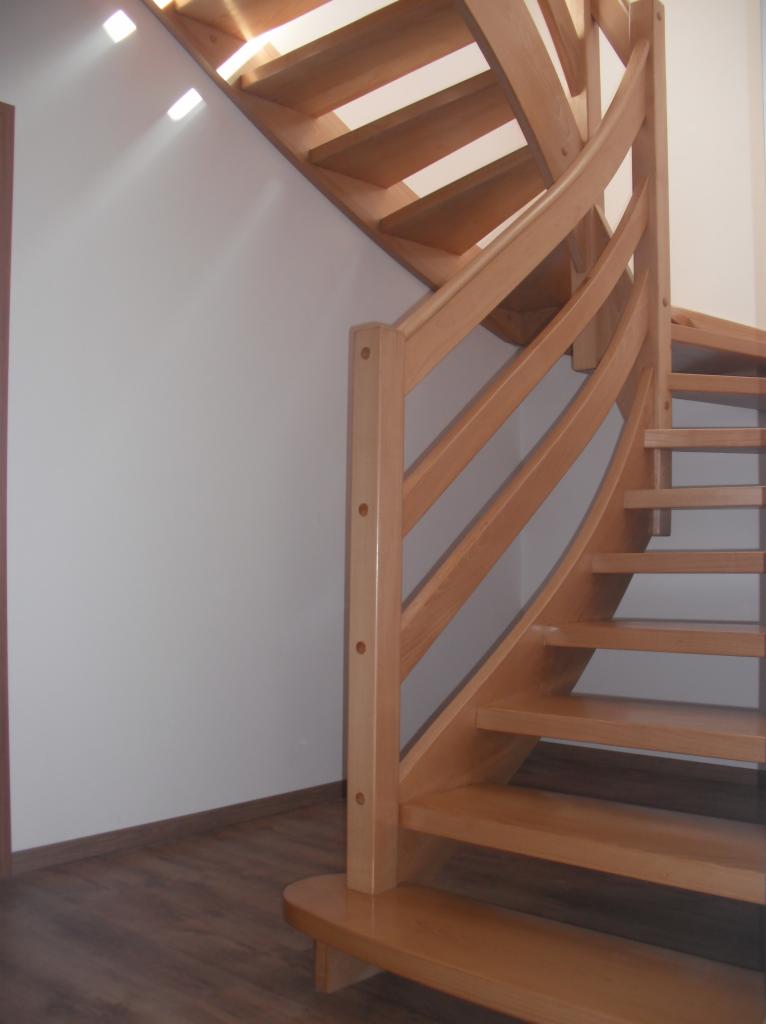 Jasne, drewniane schody spiralne z balustradą z okrągłymi szczeblami, widoczne z dołu, z podłogą imitującą drewno w tle.