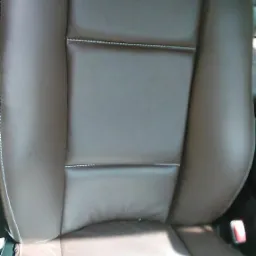 Brązowe skórzane siedzenie samochodowe z jasnymi przeszyciami, widoczne z bliska, z zagłówkiem i fragmentem pasa bezpieczeństwa.