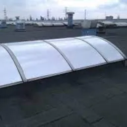 Świetlik dachowy z poliwęglanu na płaskim dachu pokrytym papą, widok z góry w pochmurny dzień.