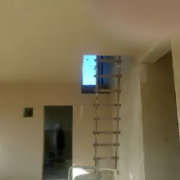 Świeżo położona gładź szpachlowa na ścianach i suficie w jasnym, pustym pomieszczeniu z drewnianą drabiną opartą o otwór w suficie, widoczne ślady po szpachlowaniu.