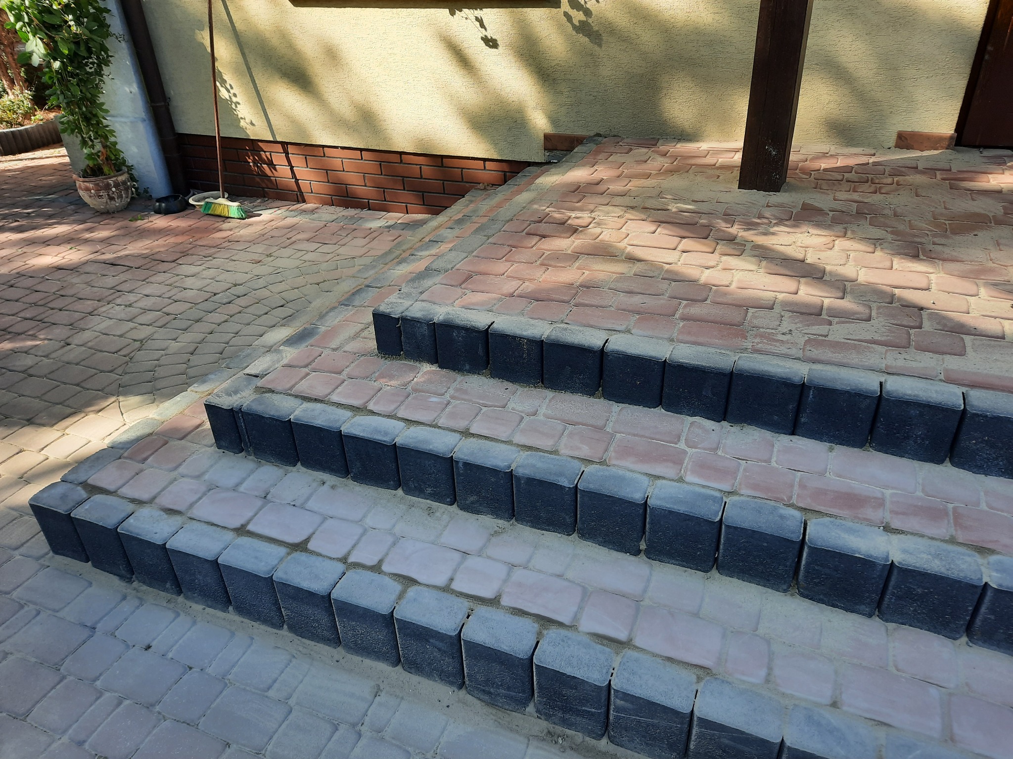 Schody wejściowe wyłożone czerwoną kostką brukową z czarnymi obrzeżami, widok z dołu, częściowo zacienione