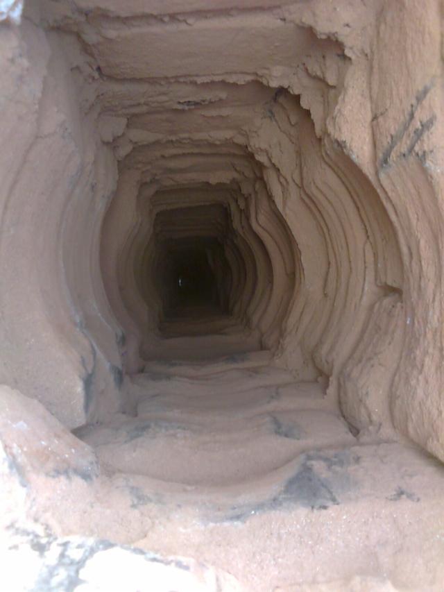 Wnętrze komina przed frezowaniem, widoczne warstwy sadzy i zanieczyszczeń, perspektywa w głąb przewodu kominowego.