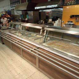 QR-Instal Robert Stwora - Nowoczesna lada chłodnicza z ekspozycją potraw w supermarkecie. Widoczne metalowe elementy, drewnopodobne wykończenie i pracownicy obsługujący klientów.