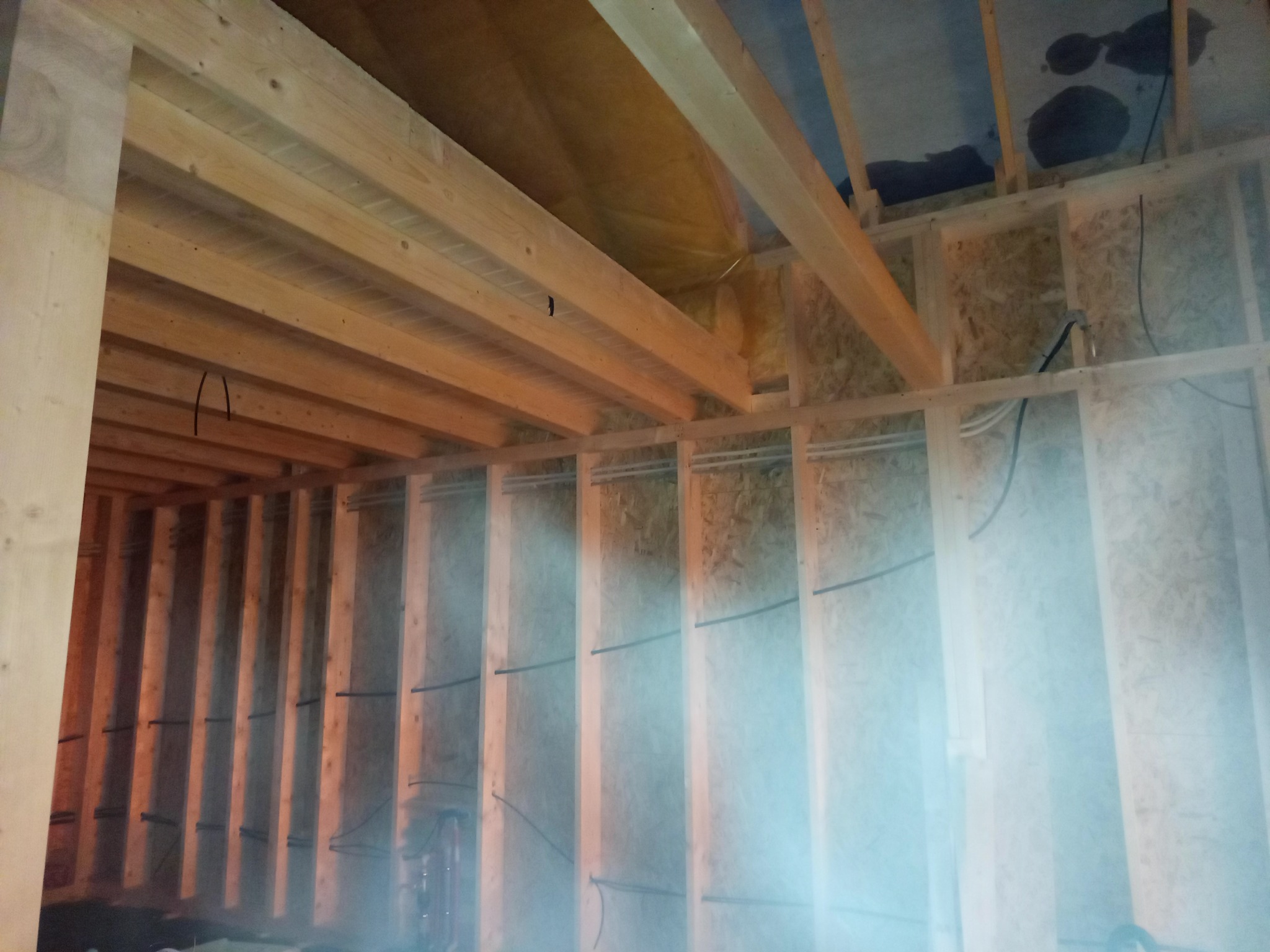 Wnętrze w trakcie budowy: drewniana konstrukcja szkieletowa ścian i stropu, widoczne przewody instalacji. Surowy stan, przygotowanie do dalszych prac wykończeniowych.