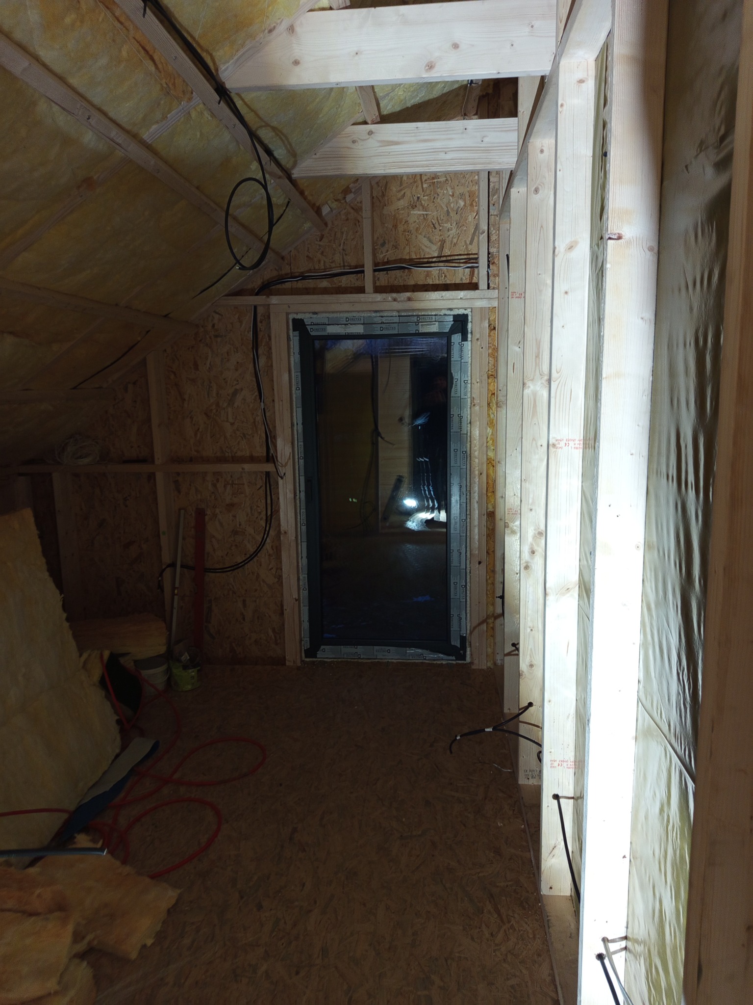 Poddasze w trakcie adaptacji: drewniana konstrukcja szkieletowa, ocieplenie wełną mineralną, widoczne przewody elektryczne. Etap prac przed wykończeniem.