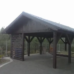 Drewniana altana z zadaszeniem i częściowo zabudowanymi ścianami bocznymi, widoczna z zewnątrz, z elementami wyposażenia wewnątrz i drabina oparta o ścianę.