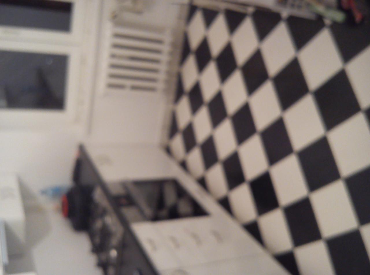 Niedokończona łazienka z czarno-białą szachownicą na ścianie, widoczne okno i fragment umywalki, zdjęcie rozmazane.