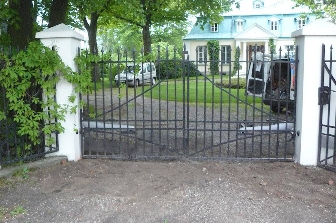 Dwuskrzydłowa brama wjazdowa z czarnego metalu, z automatyką, widoczna w tle biała rezydencja i samochód dostawczy z otwartymi drzwiami.